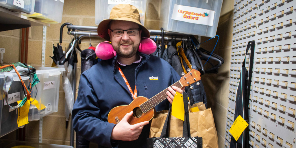 A man smiling holding a guitar and surrounded by various objects