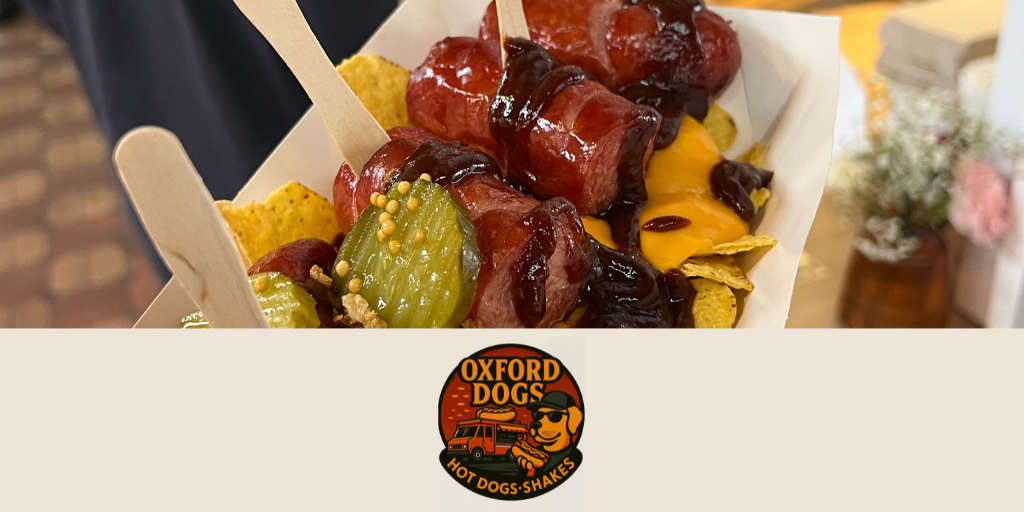 The image depicts a French-style sausage topped with gherkins and sauce. Below the photograph, the logo of the food outlet "Oxford Dogs" is displayed below.